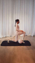 Frau in rosa Sportoutfit macht einen Ausfallschritt auf einer Yogamatte mit kleinem Pilates-Ball, trägt Studio Élancé Socken